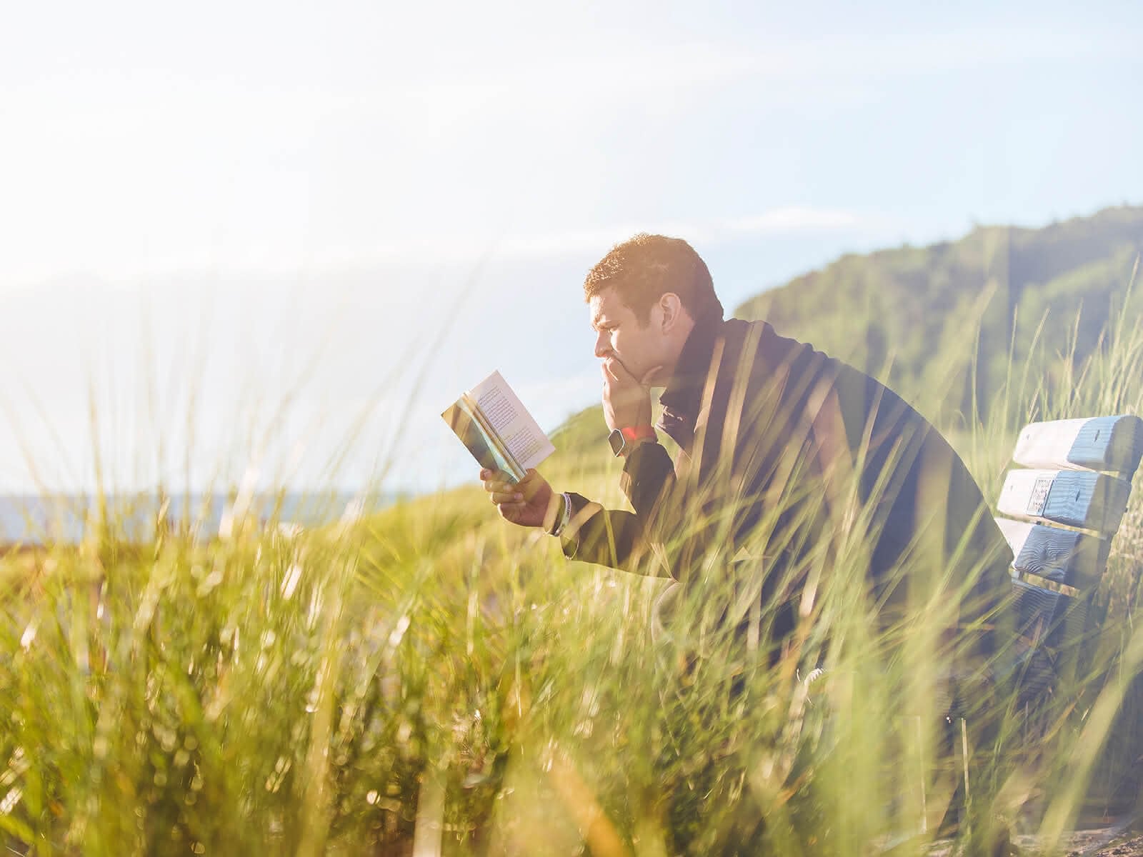 Mann mit Buch auf einer Bank in einer Wiese