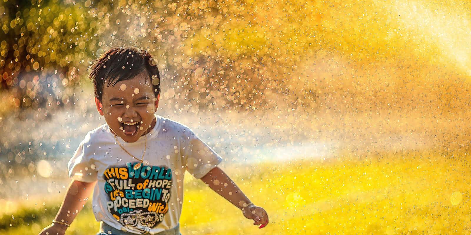 Kleiner Junge läuft durch das Wasser vom Rasensprenger